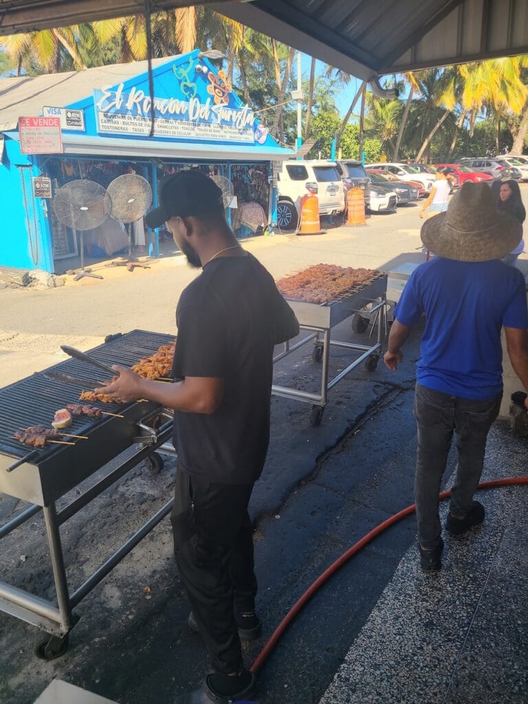 Cook grilling skewers of meat at an outdoor roadside food stand