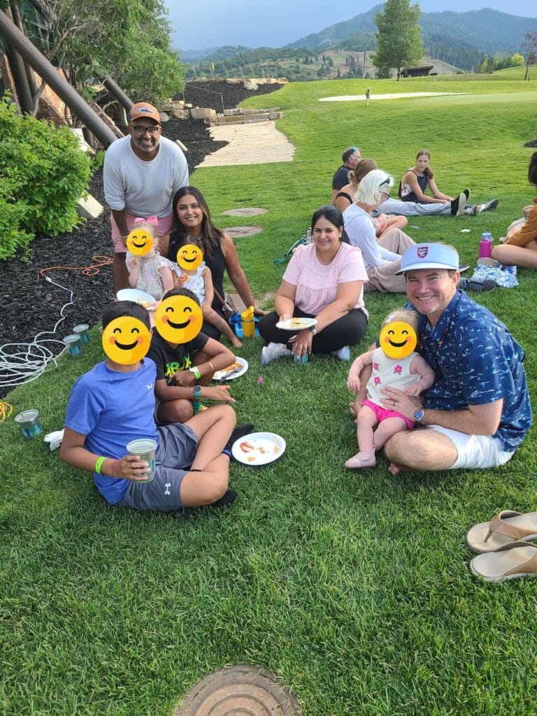 Families gathered on a grassy lawn at an outdoor event with mountains in the background